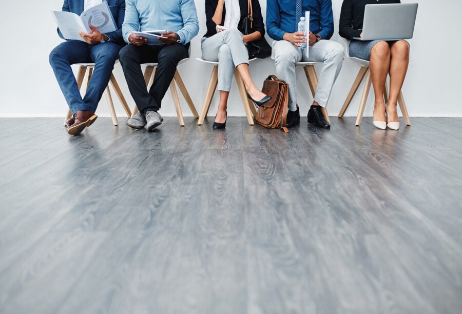 A group people sitting in a row waiting for an interview with their faces cropped out of the shot