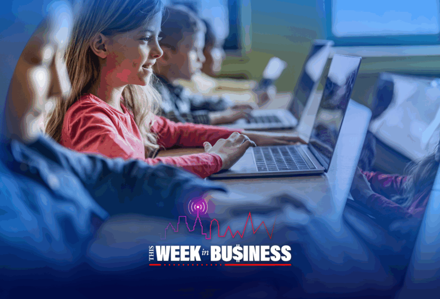 Children sitting in a classroom using laptops, with "This Week in Business" written at the bottom.
