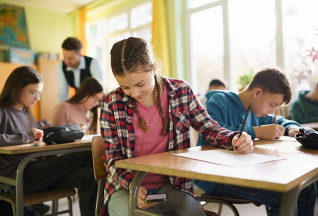 Teenage girl using a smart phone during an exam in the classroom