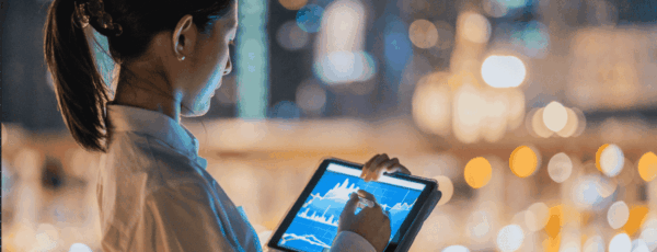 A person wearing a white shirt using a tablet with graphs, against a blurred urban nightscape.