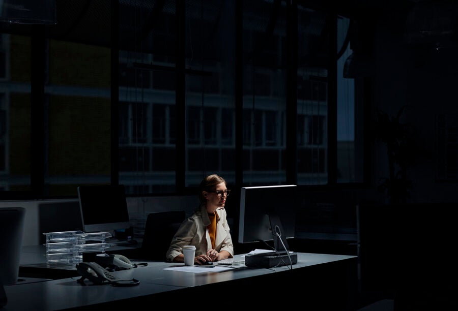 A person working late at night in a dimly lit office, illuminated by a computer monitor.
